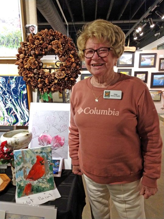 Woman displaying artwork at gallery exhibit.