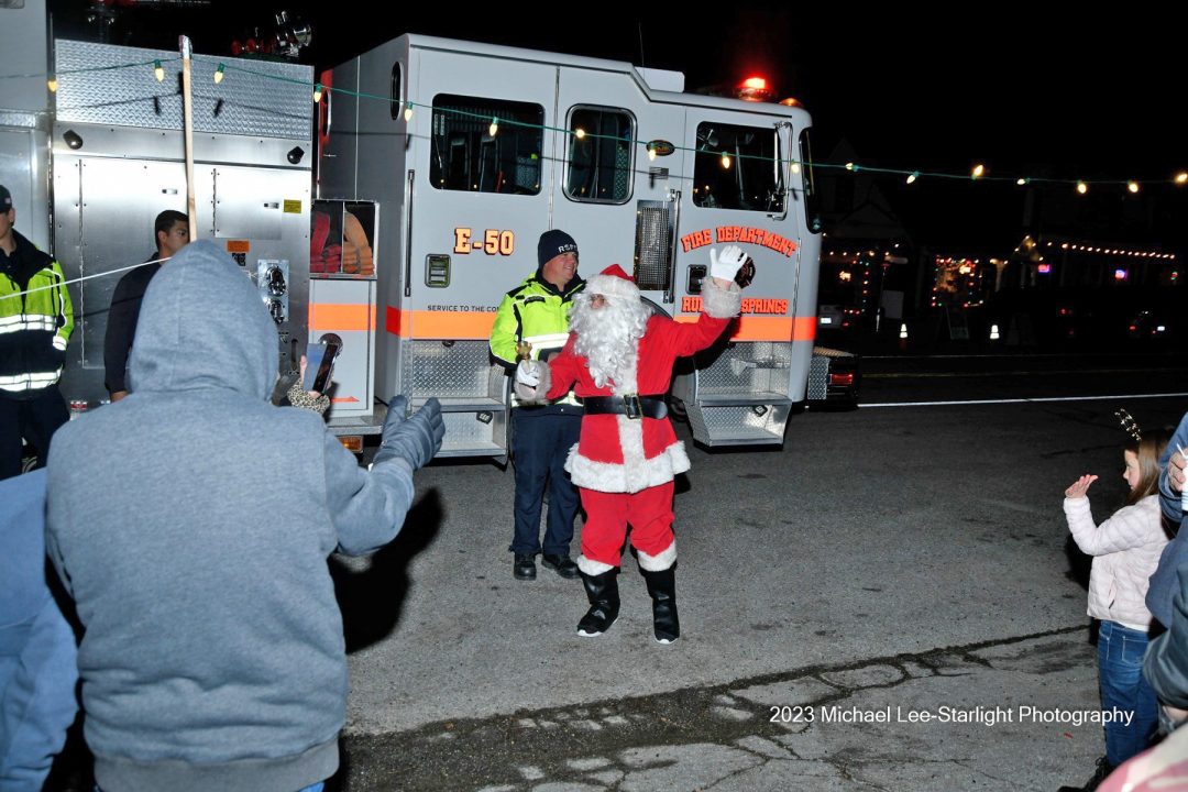 Santa waving near fire truck at night event.