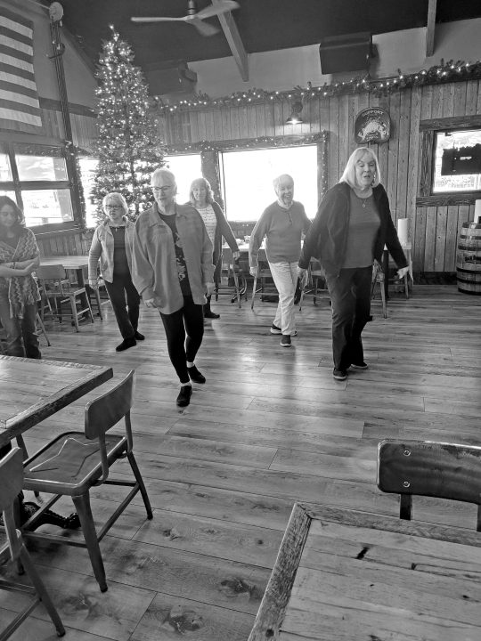 Group line dancing in festive decorated room.