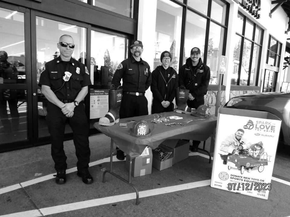 Firefighters promoting toy drive outside store.