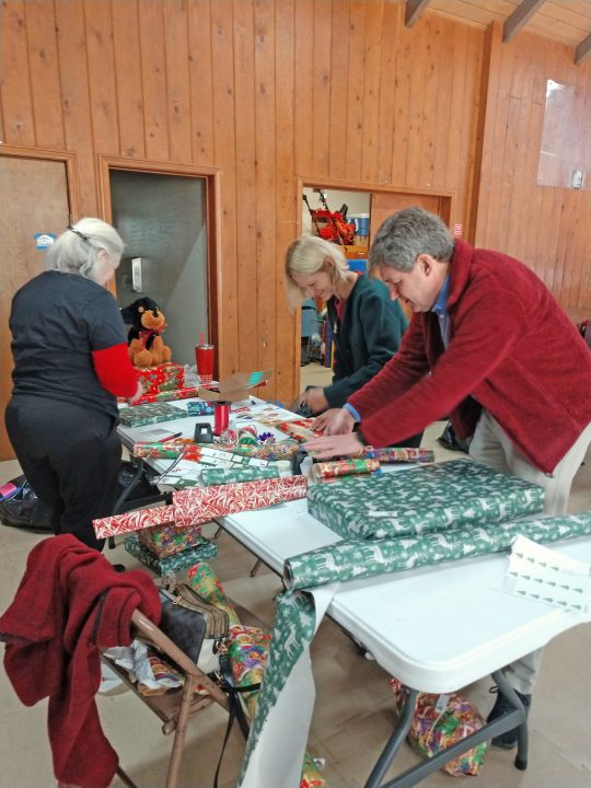 Three people wrapping gifts at a table.