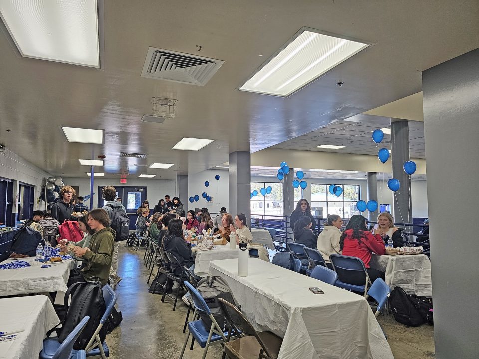 Students gathered in cafeteria for event with blue balloons.