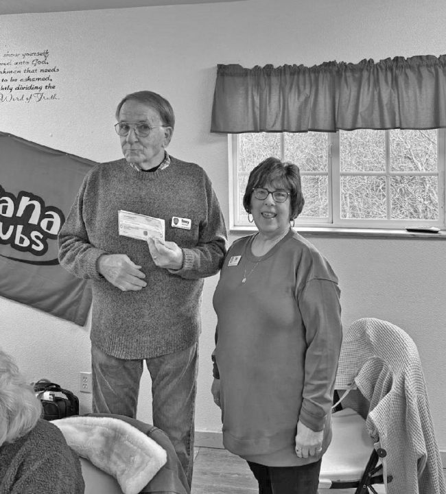 Smiling couple with check indoors, club banner visible.