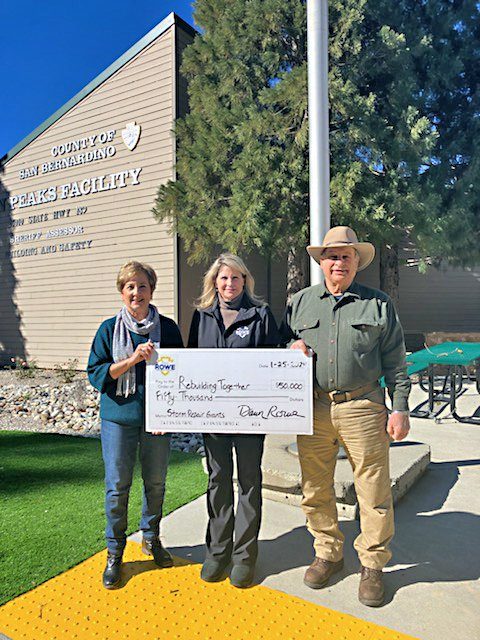 Three people holding $50,000 check outside facility.