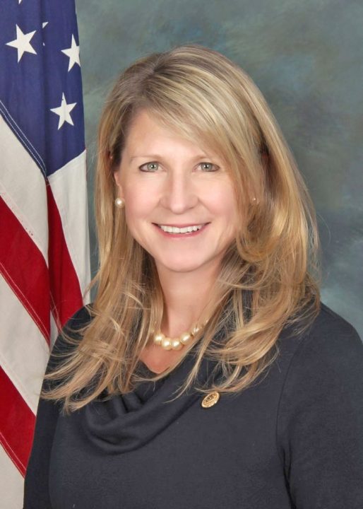 Person smiling in front of American flag.
