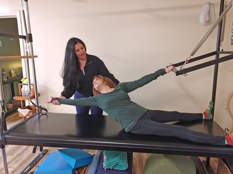 Melissa Post works with client Gloria Wolen, who is doing a side reach on the Pilates Cadillac reformer. (Photo by Mary-Justine Lanyon)