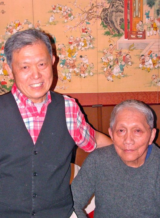 Two men smiling in front of decorative screen