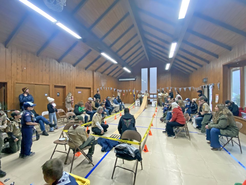 Indoor pinewood derby race with spectators watching.