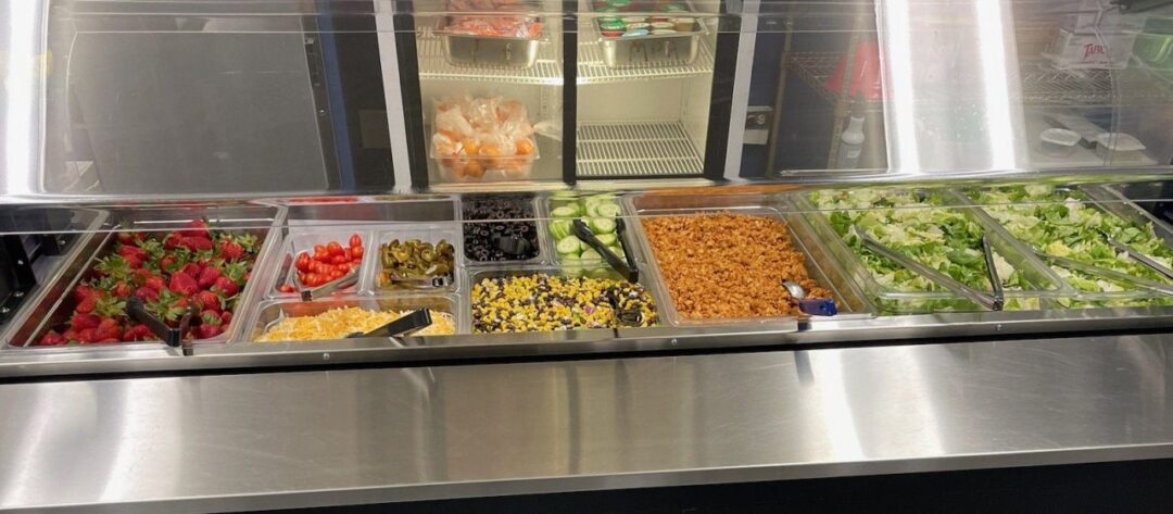 Salad bar with fresh vegetables and toppings.