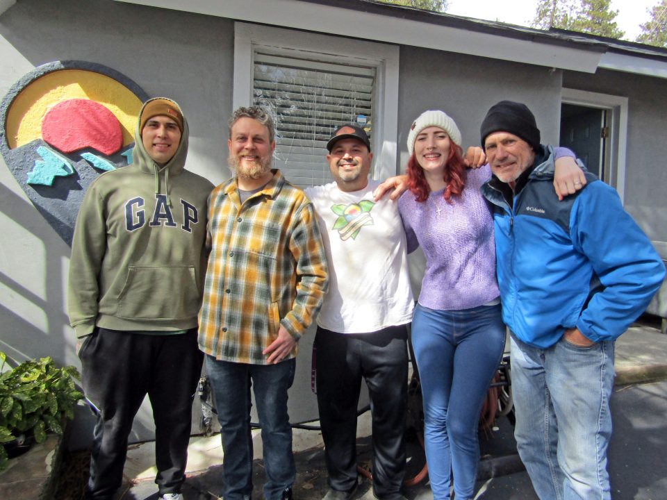 Group of five people smiling outside a house.