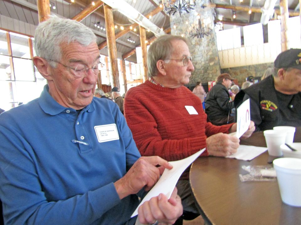 Elderly men reviewing documents at a gathering.