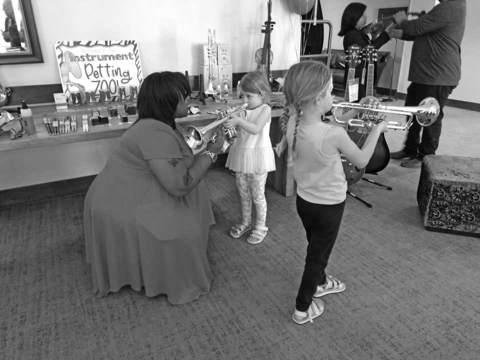 Karissa from Music & Arts helped Bellamy, 7, and her sister, Kensington, 4, blow some notes with trumpets from the instrument “petting zoo.”