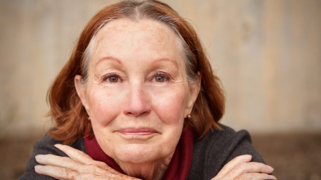 Elderly woman with a scarf smiling gently.