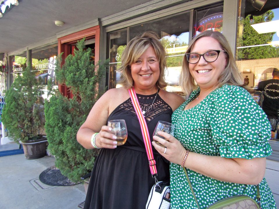 Two women smiling with drinks outside a shop