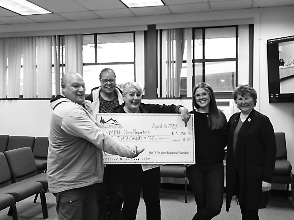 Group holding a large check indoors, smiling.