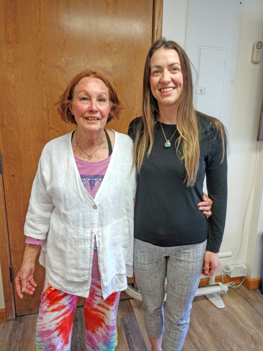 Two smiling women standing together indoors.