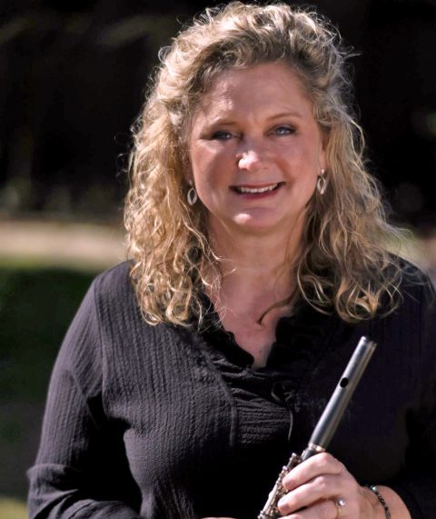 Woman smiling, holding a flute outdoors