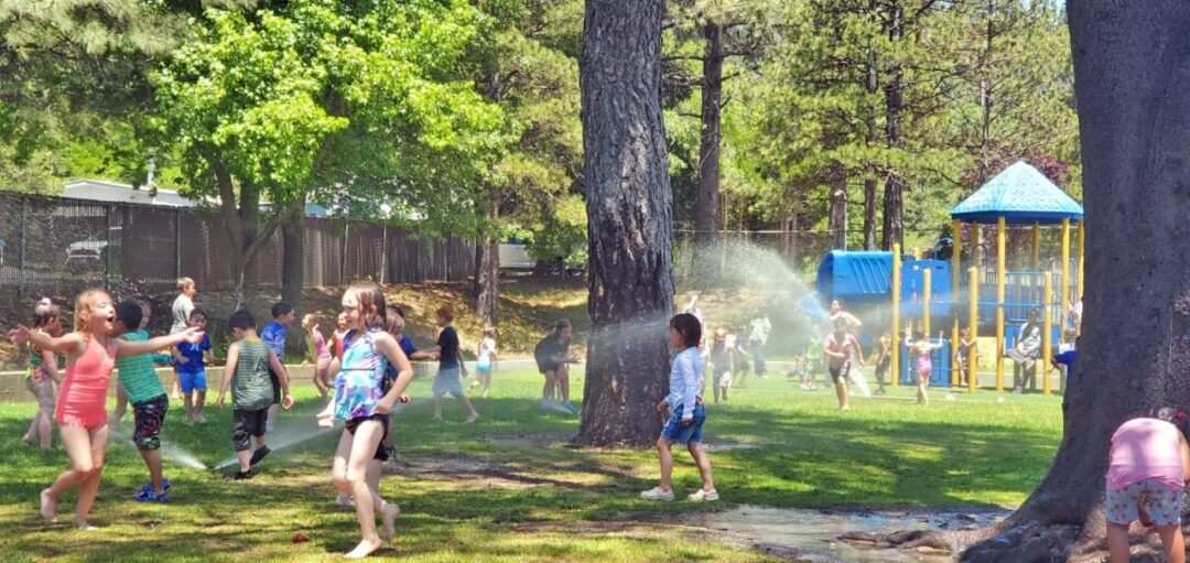 Kids playing in park with playground and water sprinklers.