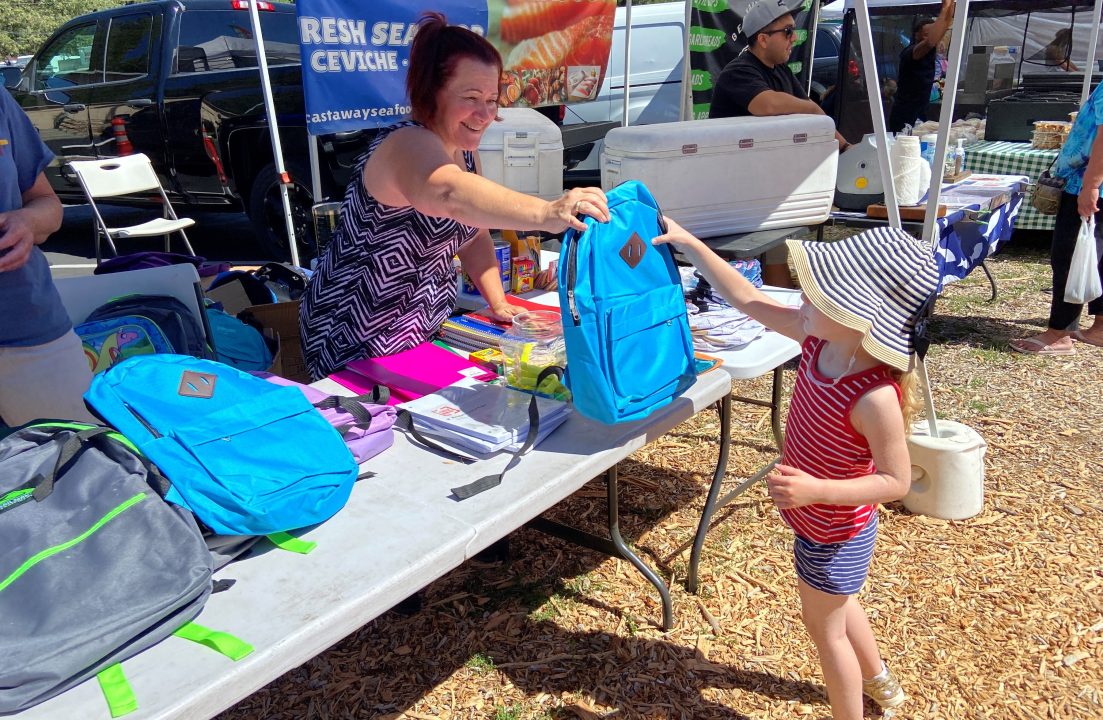 Vendor giving backpack to child at market.