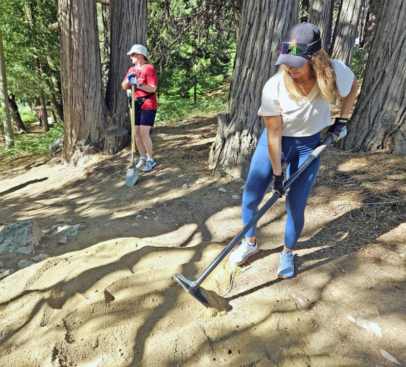 Two people maintaining forest trail with tools.