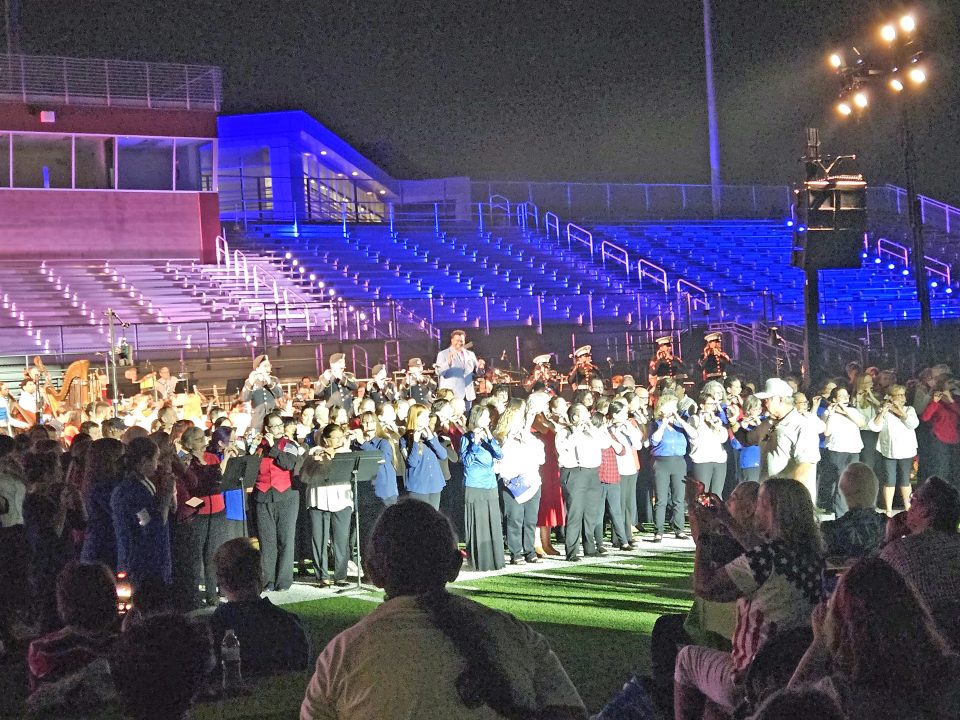 Large choir performs at illuminated stadium event.