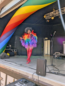 Drag queen performs under rainbow arch on stage.