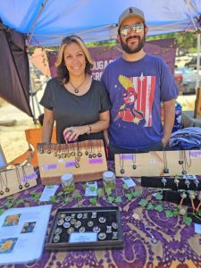 Two vendors selling handmade jewelry at outdoor market.