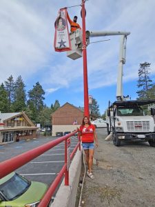 With Mickey Flores-Caballero standing below, Josh Snyder hangs her son Jared Moore’s banner by the bowling alley in Crestline.