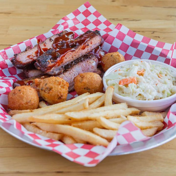 Barbecue ribs, fries, coleslaw, hushpuppies on checkered paper.