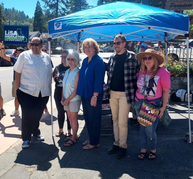 Group standing under a blue canopy at outdoor event.