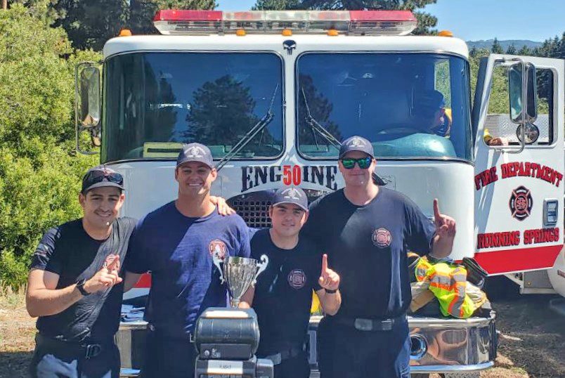 Firefighters posing with trophy in front of fire engine.