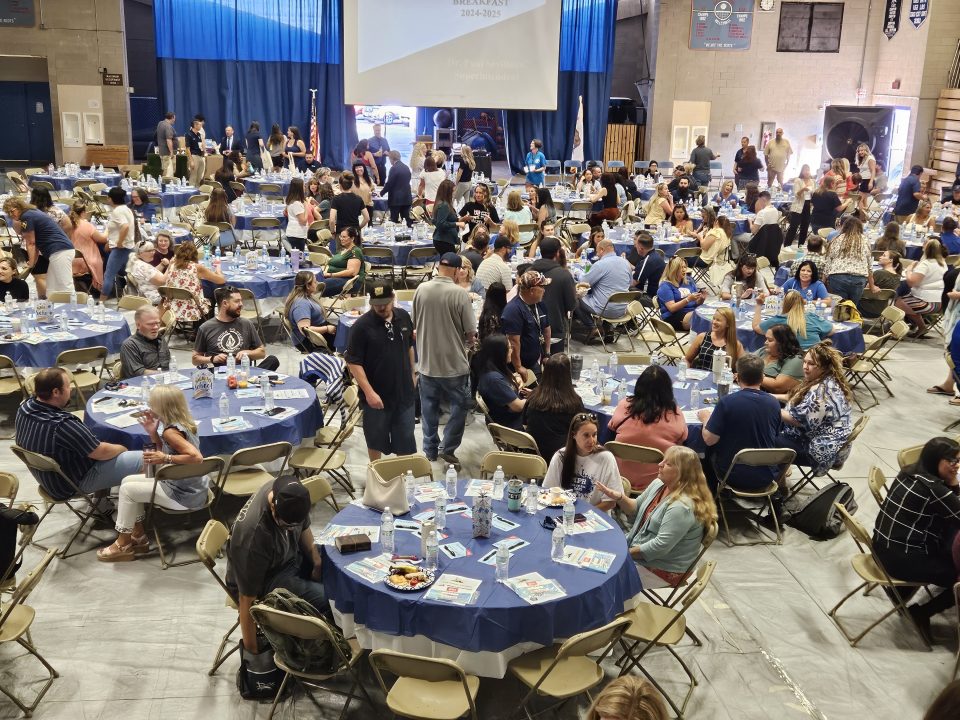 People gathering at indoor event with tables and chairs.