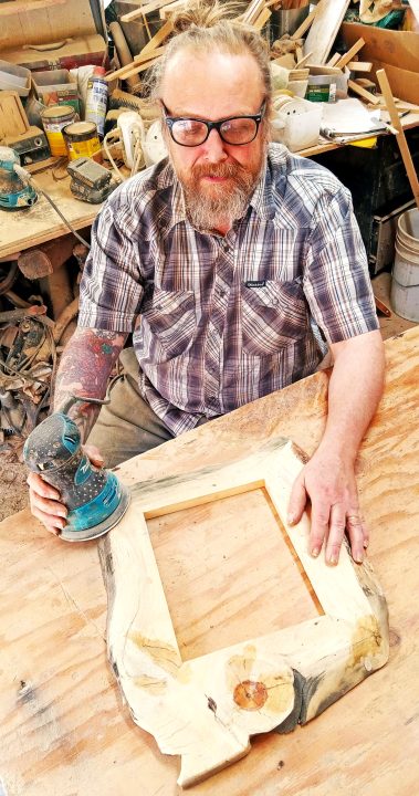 The artist invests hours every day in his garage workshop. Here he’s using an orbital sander to finish a sugar-pine frame. (Photo by T. Wilcox)