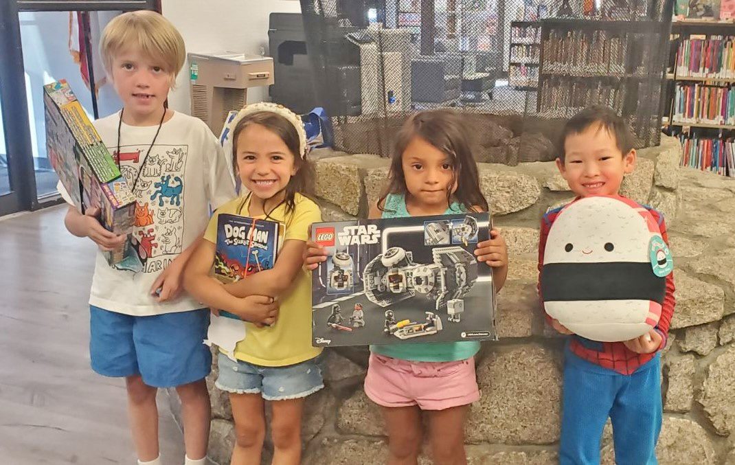 Children excitedly displaying toys and books in library.