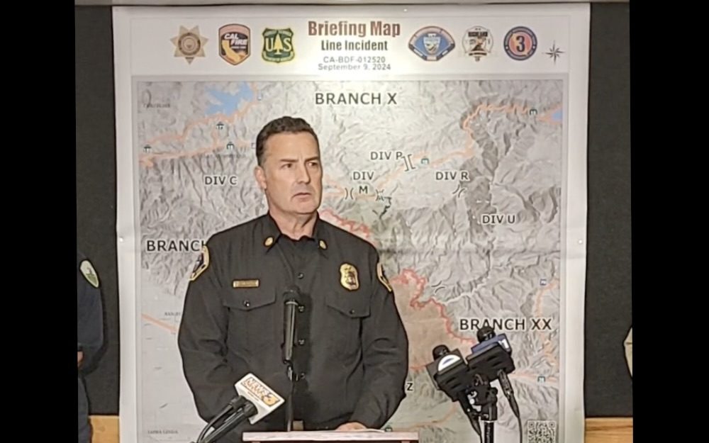 Fire official giving briefing with incident map background.