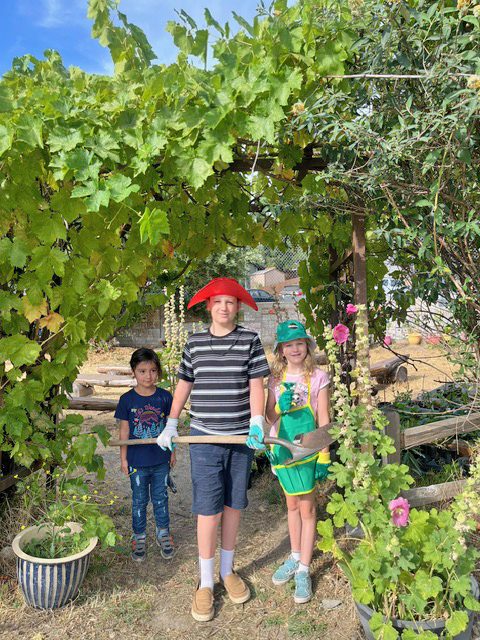 Three kids gardening under a leafy archway.
