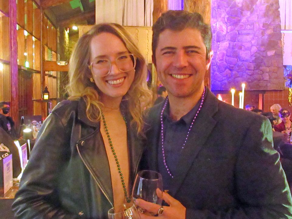 Smiling couple at a party with wine glasses.
