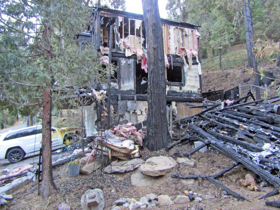 Burned-down house with debris and trees surrounding it.