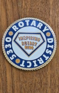 Rotary District Inspiring Hero badge on wood background.