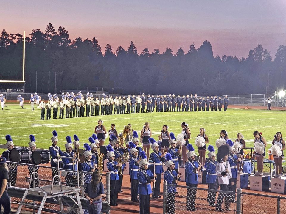Football field with band and cheerleaders at sunset.