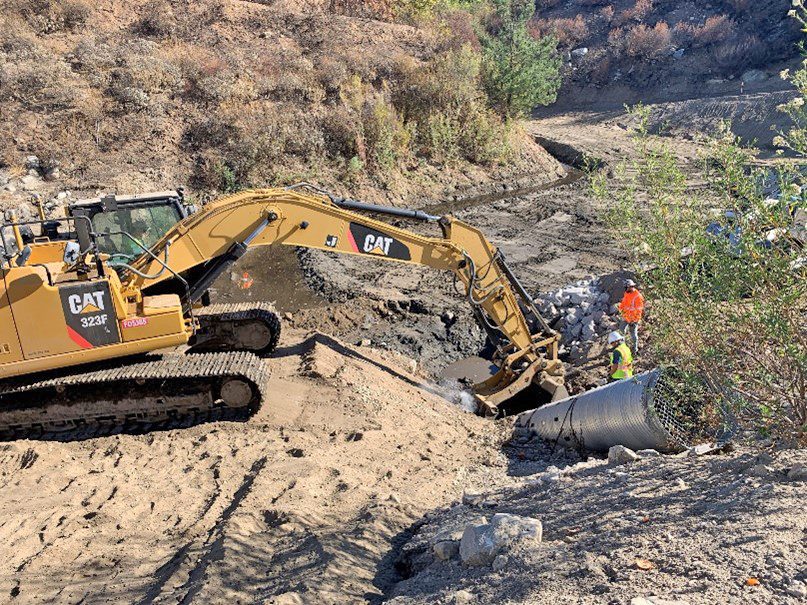 Excavator clearing soil near large drainage pipe.