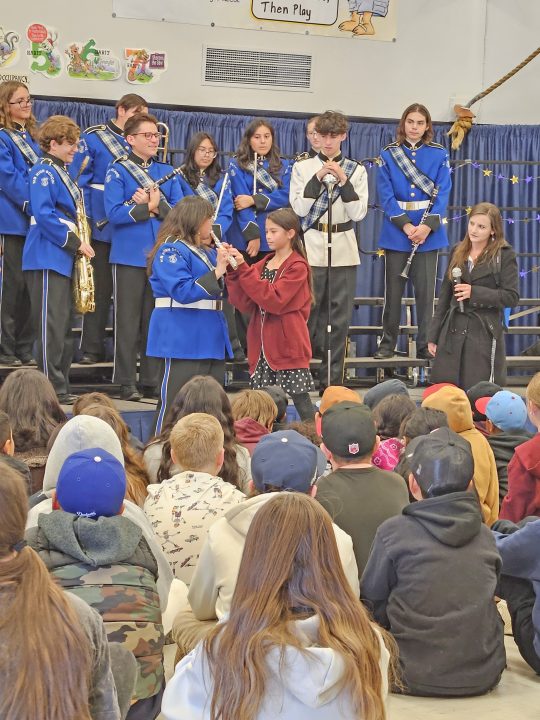 Evy, who plays the flute, presses the keys on Avrie’s flute as the Marching Scot blows across the mouthpiece.