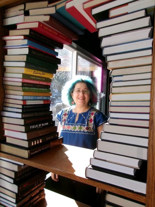 Rachel Brown through the photo frame of books in the new bookstore Paper & Clay in Lake Gregory Village, Crestline.
