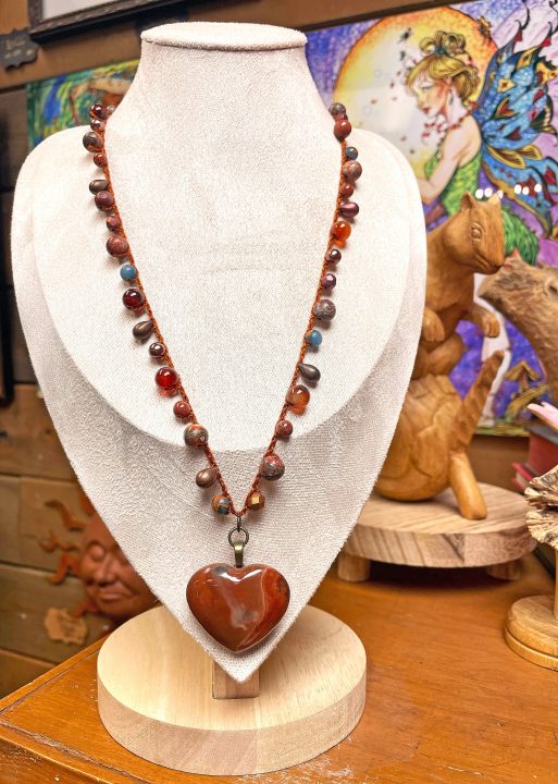 A crocheted necklace with semiprecious-stone beads supports a polychrome-jasper heart pendant. In the background is one of husband John’s Romantasy illustrations. (Photos courtesy of Romantasy Jewelry and Mystwood Gallery)