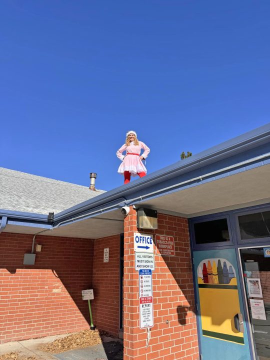 Person in costume stands on building roof.