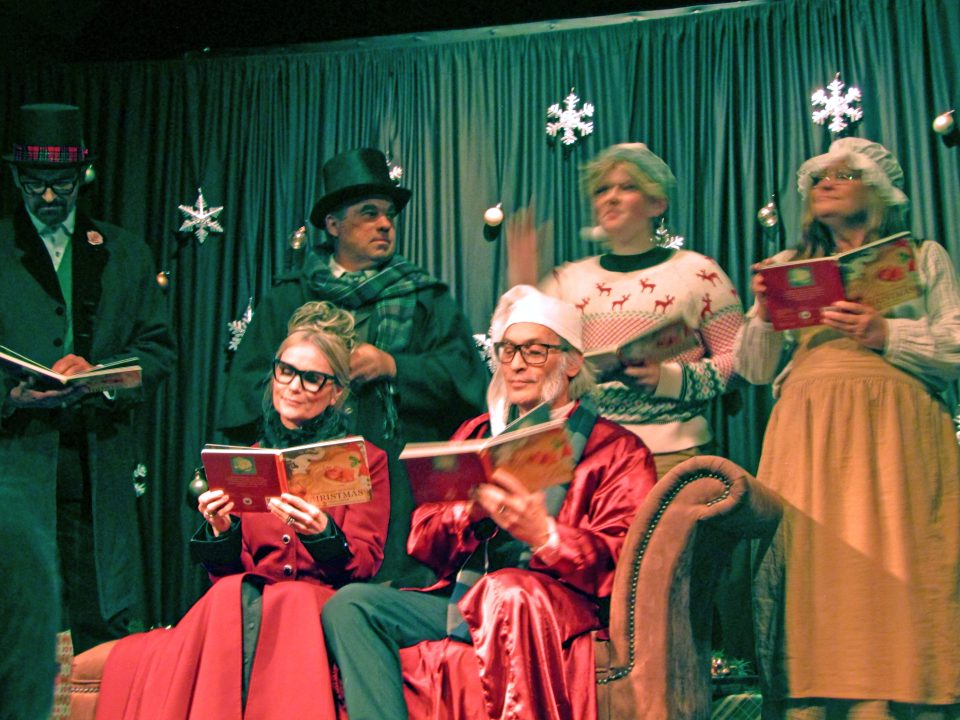 Actors in Christmas costumes reading on stage.