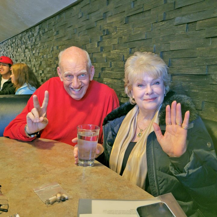 Smiling couple sitting at a restaurant table, waving.