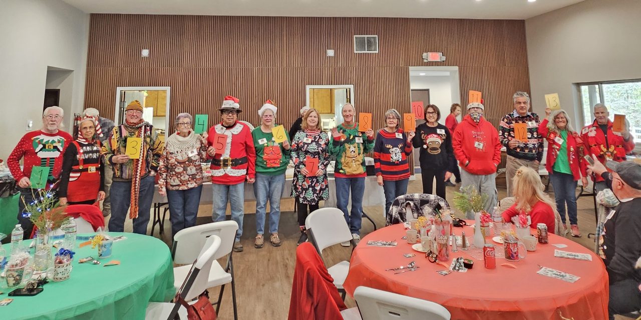 Group wearing festive Christmas sweaters holding numbered cards.