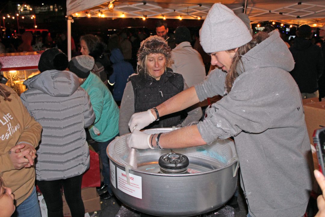 Gabriel Shore from New Life Christian Fellowship spins another cotton candy treat for visitors as Gayle Nollan, center, her hair covered with cotton candy, watches. (Photo by Mike Harris)