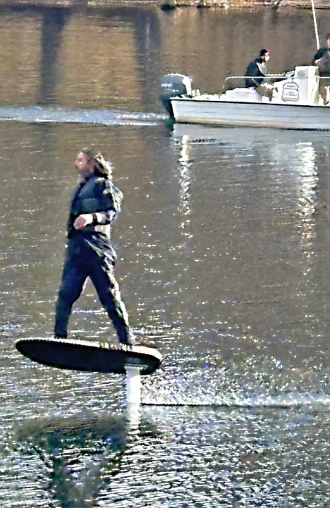 Person hydrofoiling on water near a boat.